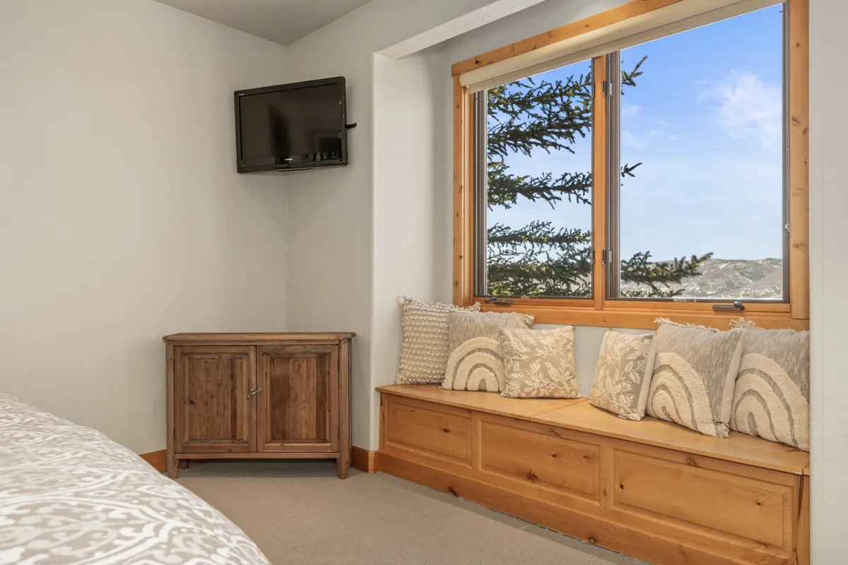 A tranquil window-side seating area with a wooden cabinet and television, offering a comfortable spot to relax, read, or enjoy expansive views after a day outside.