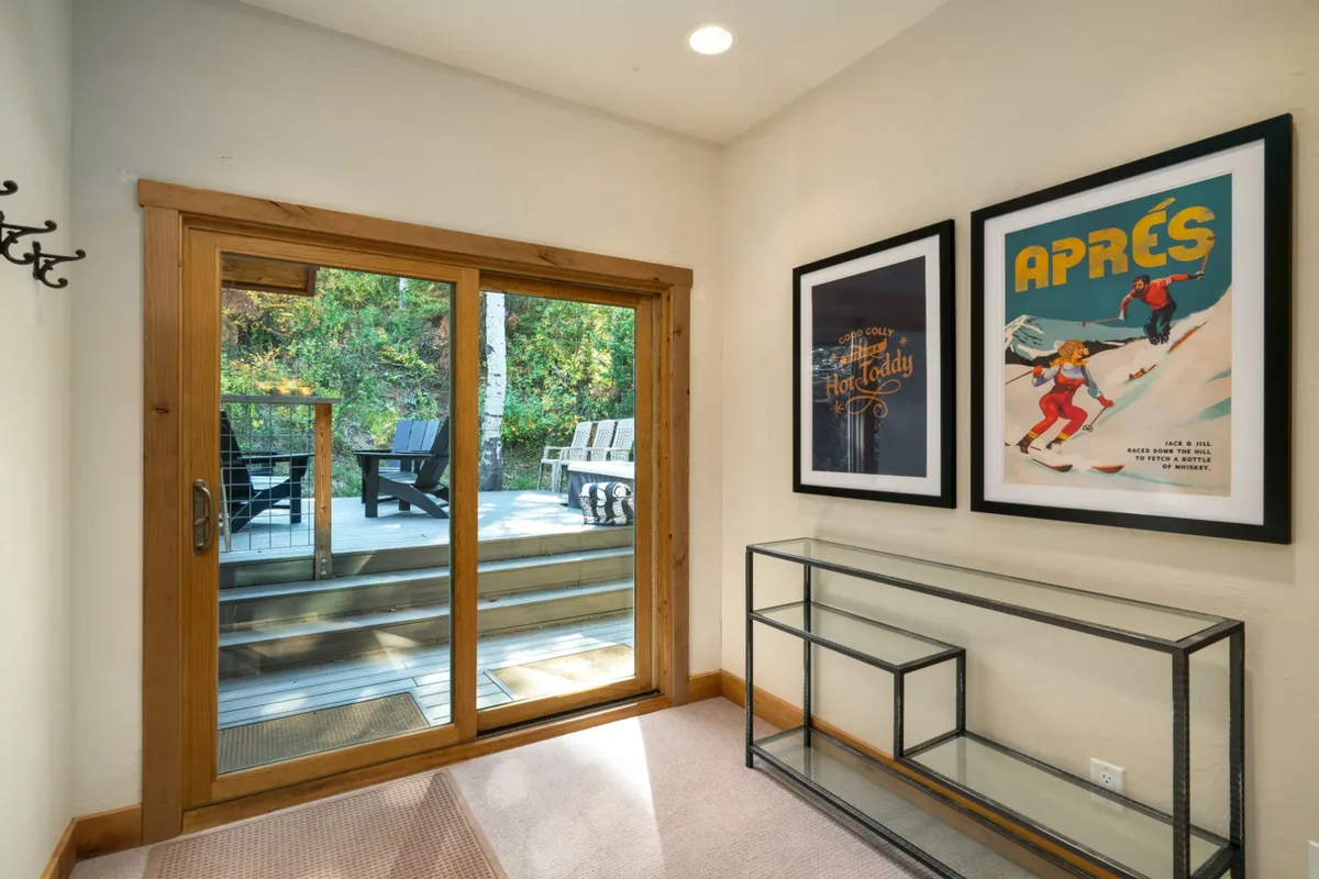 A space anchored by a glass sliding door, with framed posters and a console table, basking in natural light. The scene suggests an easy flow between indoor relaxation and stepping outside for fresh air and activities.