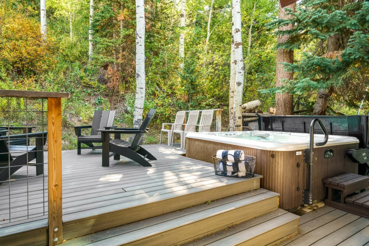A tranquil outdoor hot tub sits on a multi-level deck surrounded by trees, with comfortable seating and nature all around. The hot tub area looks peaceful and inviting, perfect for morning relaxation or evening stargazing.