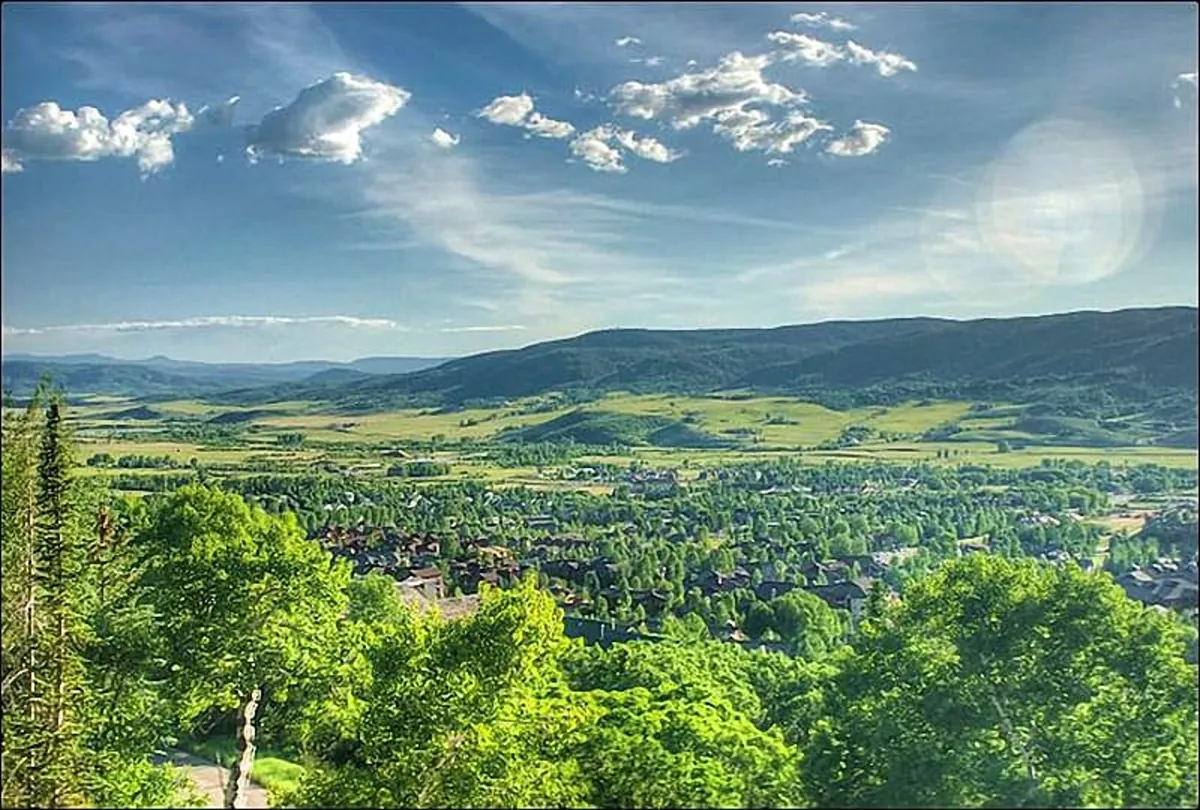 A panoramic view of vibrant green trees, rolling hills, distant mountains, and the quaint town in the valley below. The landscape captures the region's scenic playground and hints at the year-round outdoor activities available.
