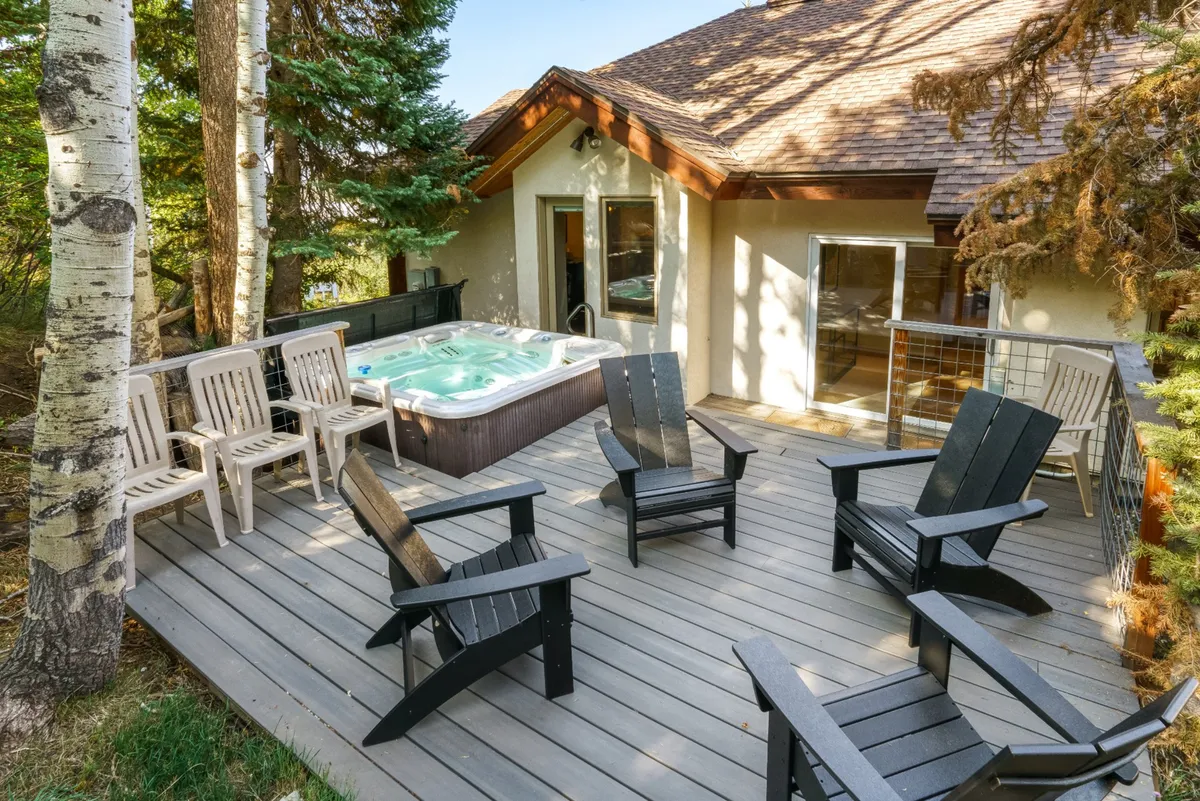 An inviting outdoor deck featuring a bubbling hot tub, surrounded by Adirondack chairs and nestled among mature trees. The scene hints at relaxation and togetherness with the backdrop of natural beauty, perfect for unwinding after a day of adventure.