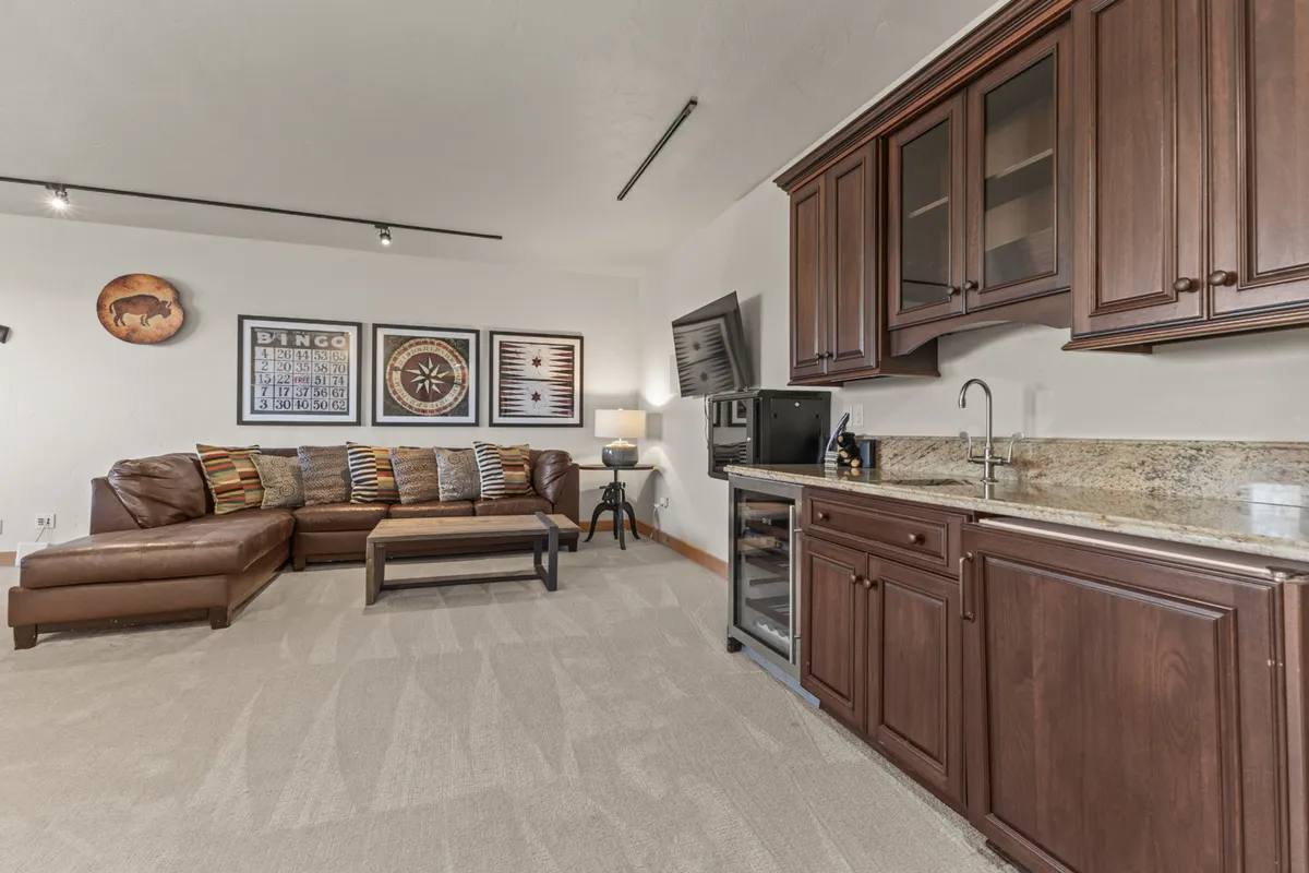 A cozy lounge area with a large sectional sofa, a bar area complete with stools, artwork, and a television on the wall. The setup is perfect for movie nights, casual cocktails, and social gatherings, reflecting the game room's multi-functional design.