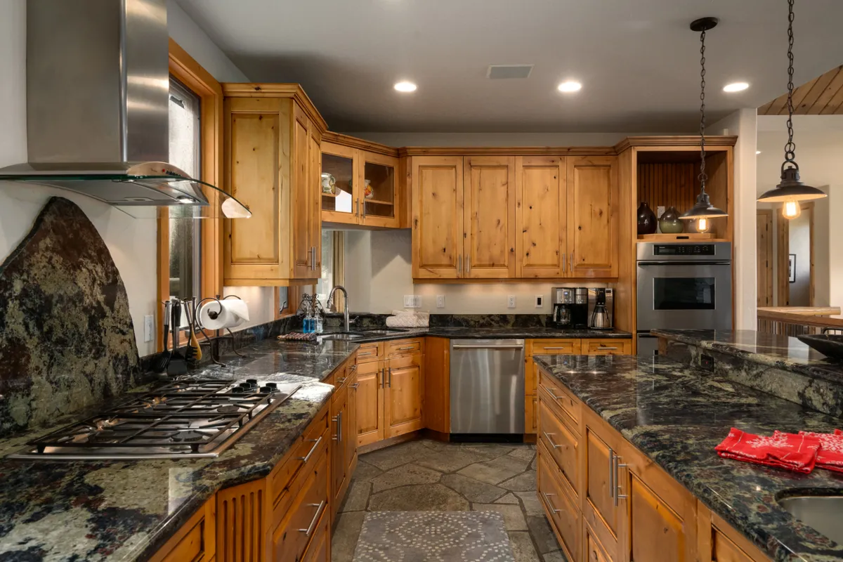 A closer look at the kitchen reveals granite countertops, rich wood cabinetry, a stylish stone backsplash, and details of high-end appliances like the professional gas range and double ovens. The kitchen island anchors the space, emphasizing its utility and elegance for culinary pursuits.