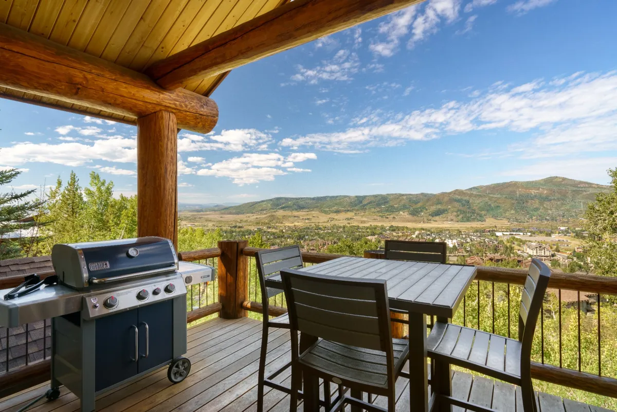 An inviting outdoor deck scene with a dining area, a BBQ grill, and sweeping mountain views—ideal for sunset cocktails or alfresco dinners. The space is seamlessly accessible from the main gathering areas, visually connecting the interior festivities with the natural landscape outside.